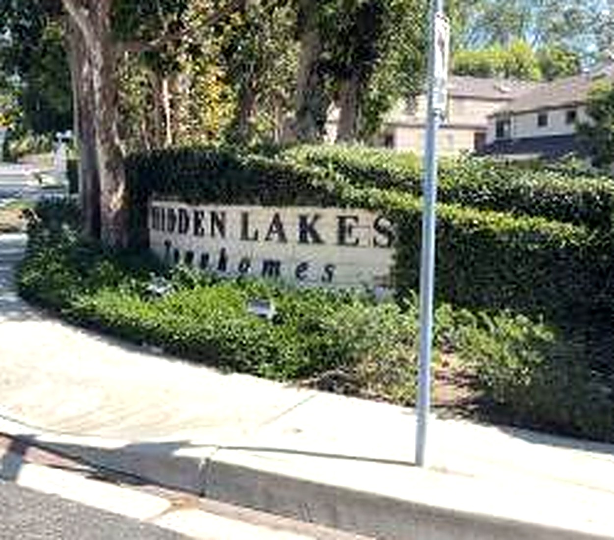 The Hidden Lakes Townhomes entrance monument at Clear Springs, framed by hedges and mature trees