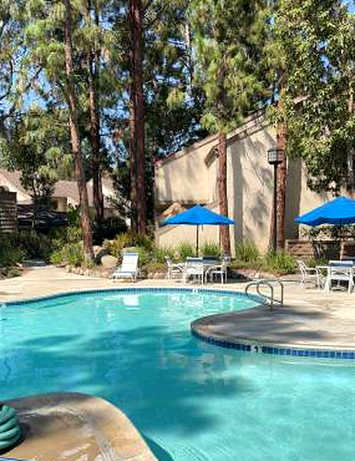 The Hidden Lakes community pool with blue umbrellas beneath tall pines